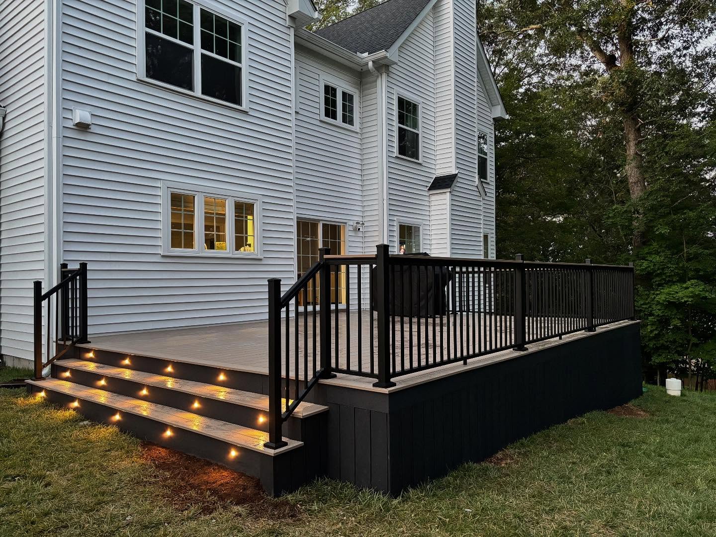 Completed composite deck with black railing and lighted stair treads at dusk, built by Mr. Deck & Patio Fairfax